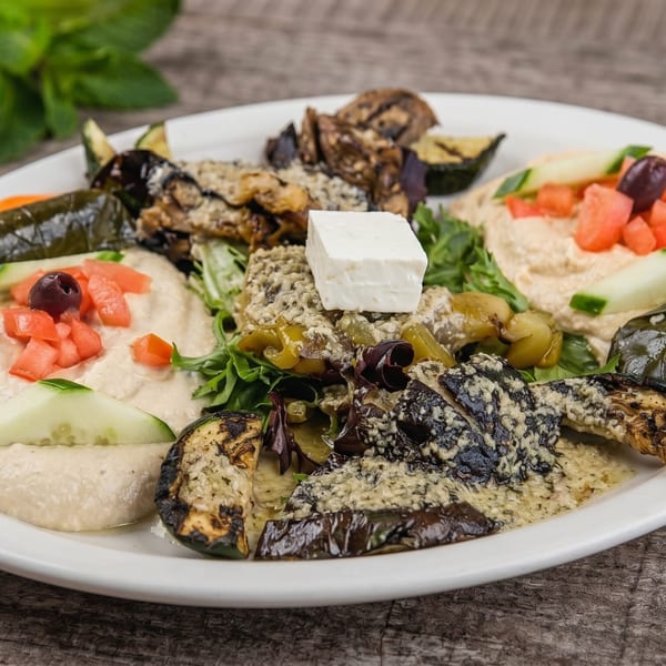 A white plate with hummus, grilled vegetables, stuffed grape leaves, and feta cheese.