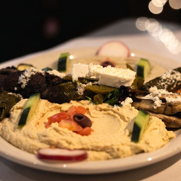 A platter of hummus, dolmades, grilled mushrooms, feta, and vegetables on a white tablecloth.
