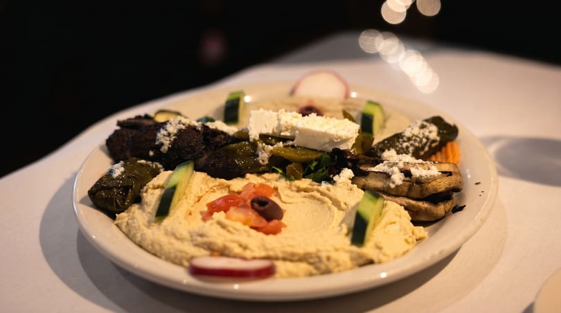 A platter of hummus, dolmades, grilled mushrooms, feta, and vegetables on a white tablecloth.